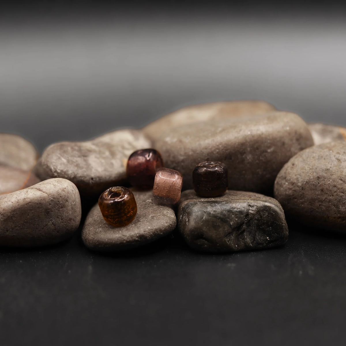 Gammallila pärlor i olika färger - brunt, lila och rosa - fotograferade på stenar för att visa material och övergripande karaktär.