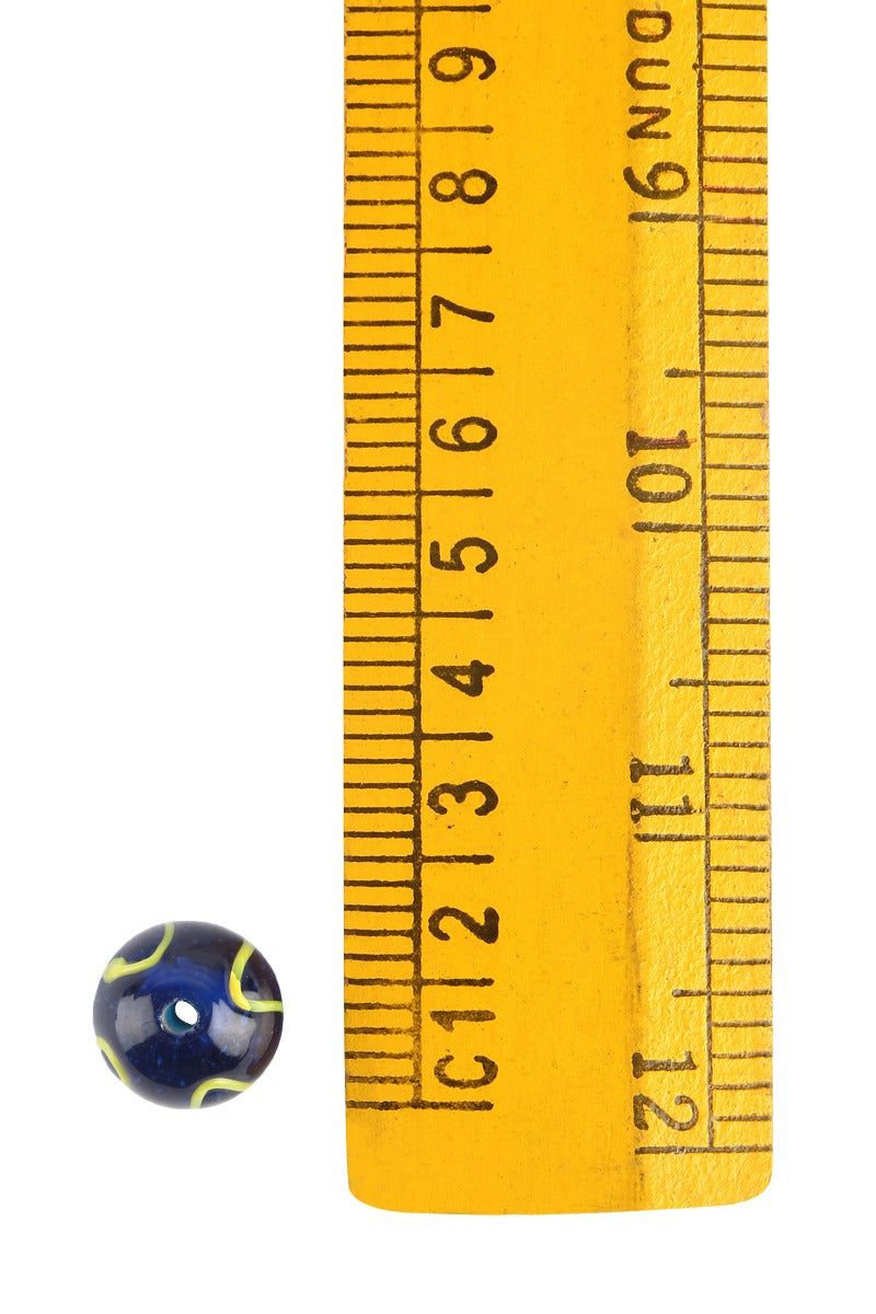 Blue glass bead with yellow wavy decoration, photographed against ruler for size reference