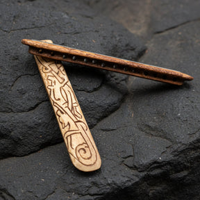 Pärlspridare av ben med vikingatida djurornamentik i närbild, liggande på mörk sten
