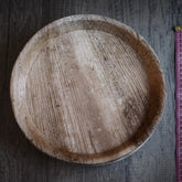 Mycket stor engångstallrik i palmblad på grå trä, fotograferad från ovan med måttlinjal för storleksreferens.