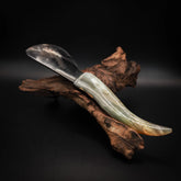 Handgjord smörkniv Freja med blankt stålblad och handtag i naturligt horn, vilande på drivved