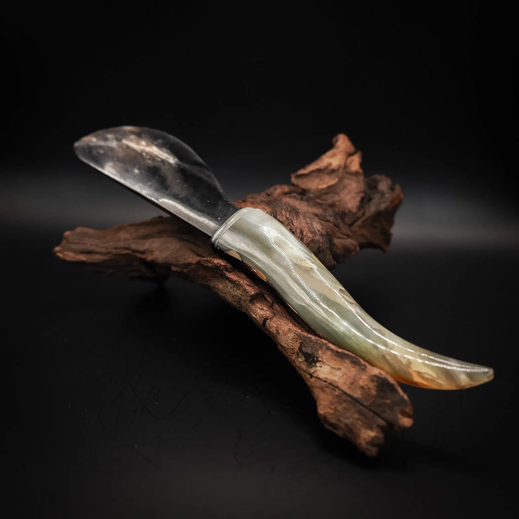 Handgjord smörkniv Freja med blankt stålblad och handtag i naturligt horn, vilande på drivved