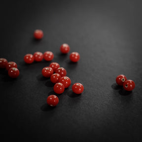 Närbild av handgjorda röda glaspärlor på svart yta, blanka och rundade med genomgående hål