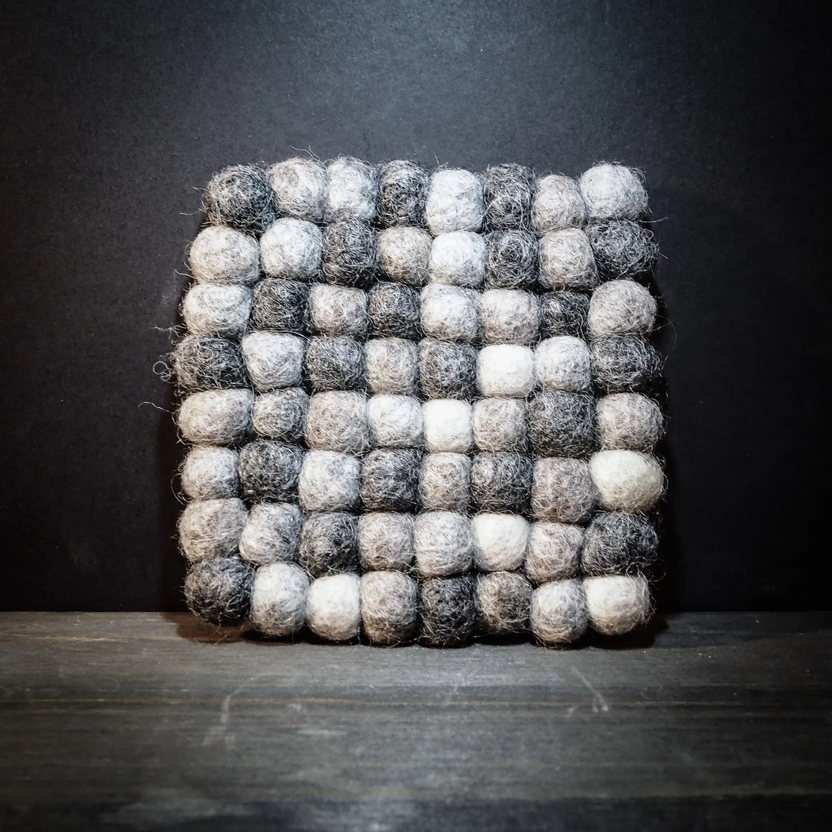 Handgjort filtrat underlägg med svart och vita ullkulor i rutnätsmönster