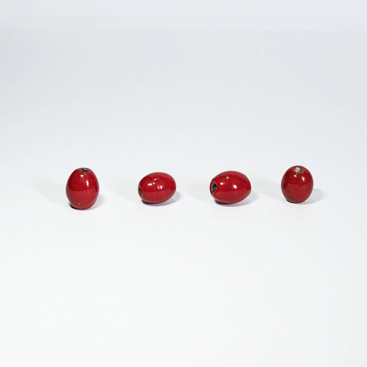 Oval rød glassperle – fire perler på lys bunn