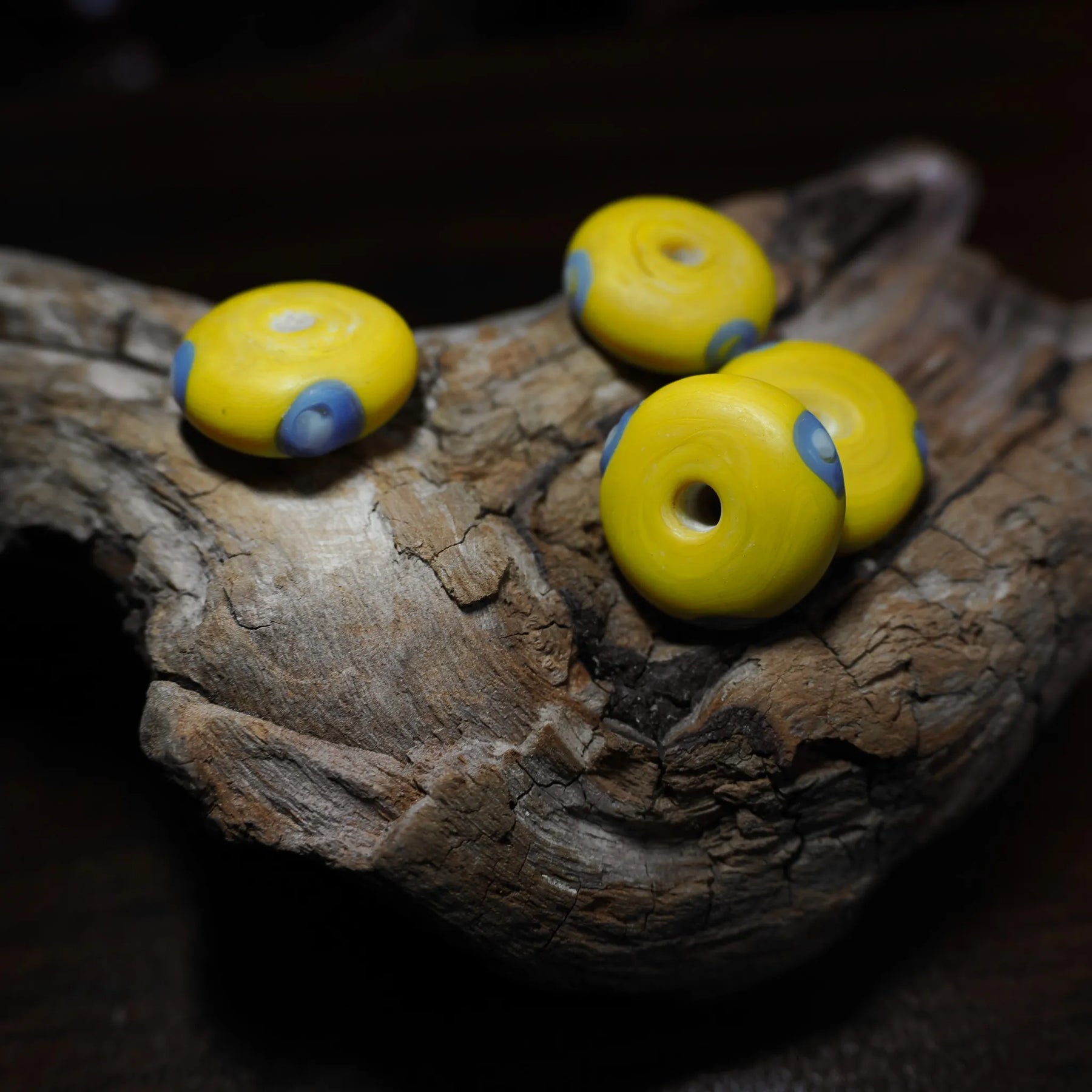 Yellow glass bead Ribe – four beads from diagonally above, blue eyes on the edge and hole in the centre