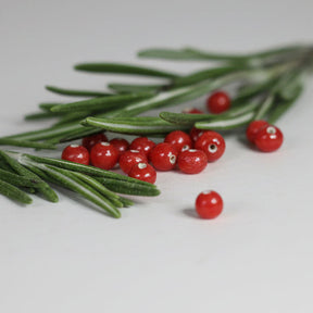 Handgjorda små röda glaspärlor från Ragnarök-serien, cirka 4mm diameter, med hål för fiskelina. Liggande på gröna barrgrenar.