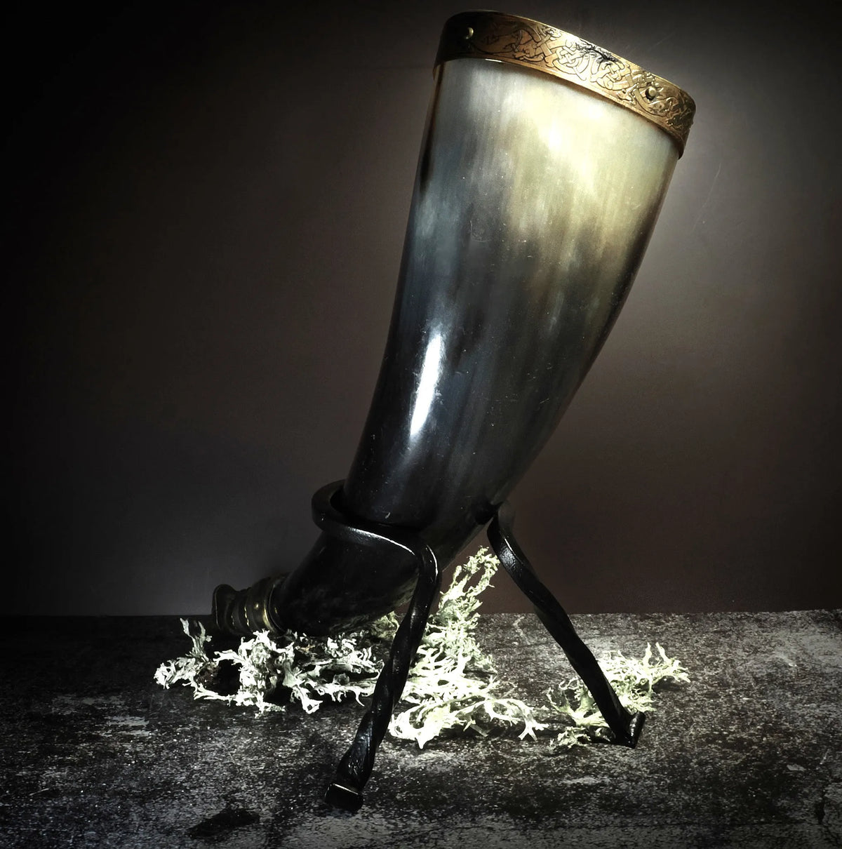 Bärsärkhorn på metallställ med tre ben, visar polerat naturhorn, mässingsdekorationer och läderwickel
