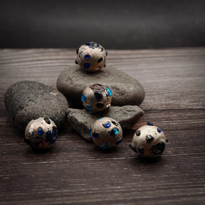 Metallisk glaspärla med turkosa prickar, 12mm diameter, på naturlig stenbakgrund för produktvisning