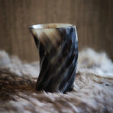 Hornglasögon med spiraldesign fotograferad framifrån, visar handsnidad vriden form med stark ljuseffekt på naturlig horn.