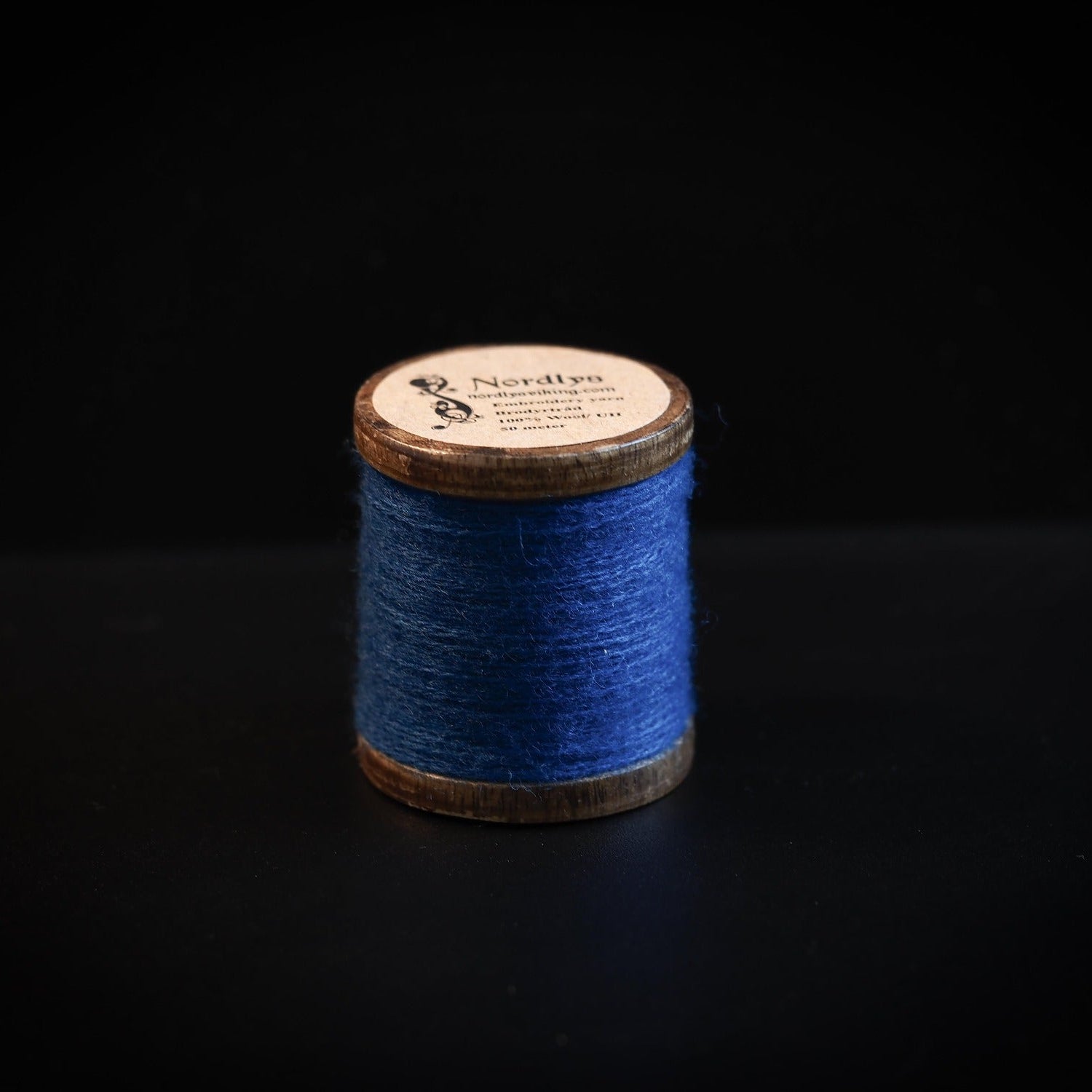 Blå brodertråd på trätrumlor med Nordlys-märkning. Klassisk träspole med handgjord look för Viking-inspirerad broderi och hantverk.