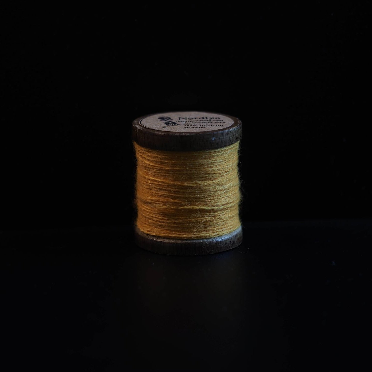 Gyllene gul-brun brodertråd på trätrumlor med Nordlys-märkning. Varm jordfärgad ton från traditionella Viking-färgämnen och naturlig växtfärgning.