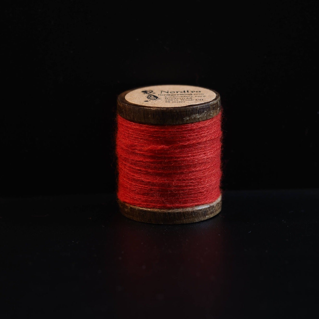 Ljus röd brodertråd på trätrumlor med Nordlys-logga. Klassisk färg för Viking-inspirerad broderi och traditionell skandinavisk textilkonst.