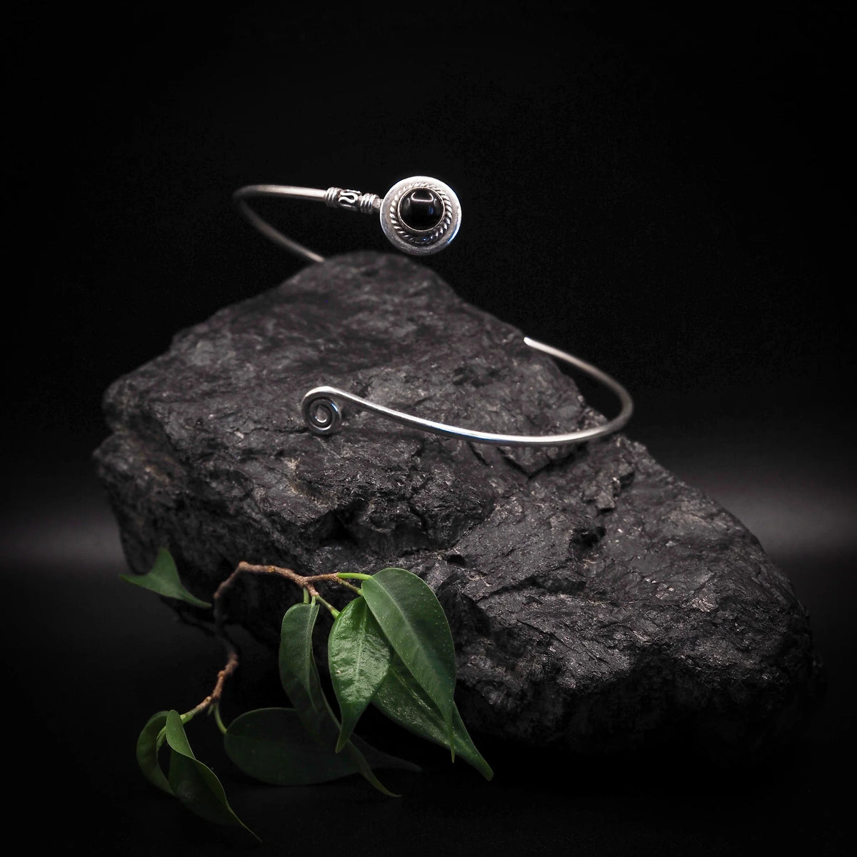 Overarmring med halvedelstein – svart stein i ringen, plassert mot mørk stein med grønne blad