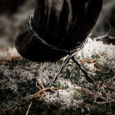 Närbild på järnsmidestall med kurvor och handverksmärken mot naturlig bakgrund med sand och lav