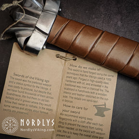 Vikingasvärd med instruktionskort och lädersvepningsdetalj.