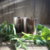 Polerte whiskyglass i horn med glatt finish på treoverflate, dekorert med grønne urter