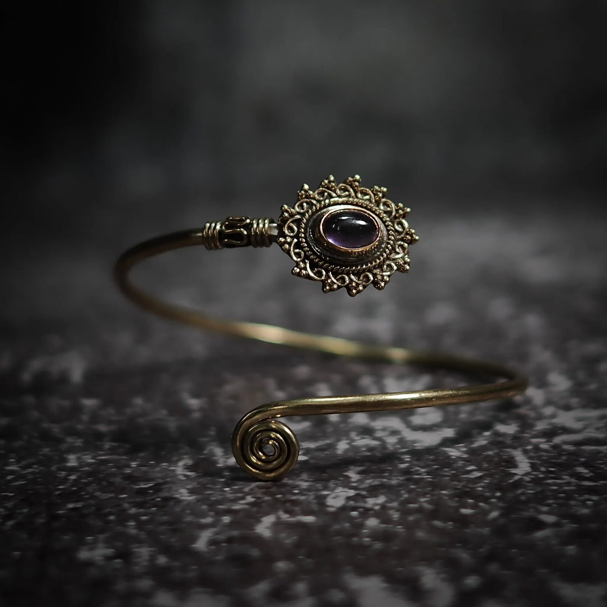 Vikingarmband i lila ametist med dekorativ mässingfiligre och spiralformad terminal på mörk sten